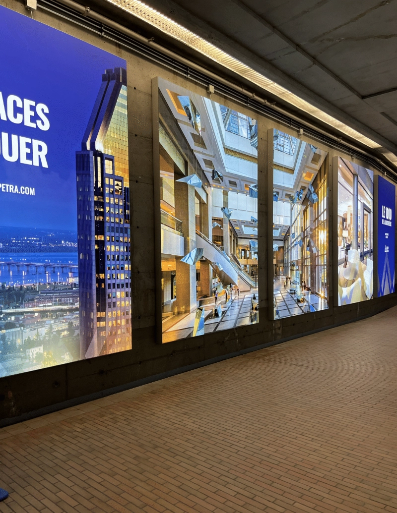 Large-format SEG lightboxes displaying real estate imagery in the underground pedestrian corridor at 1000 De La Gauchetière in Montreal.